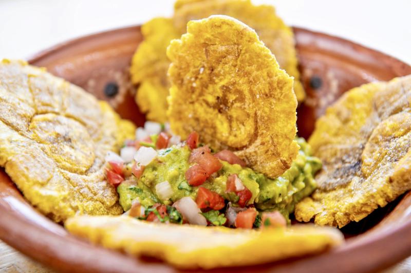 Four fried plaintain tostones with a scoop with guacamole in the middle